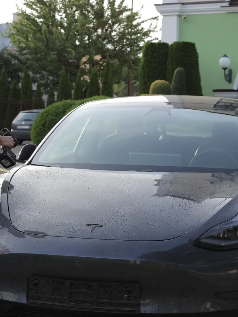 Front view of a black Tesla car parked outside, with water droplets on the hood.