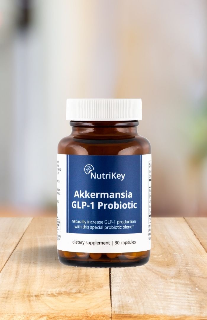 A bottle of NutriKey Akkermansia GLP-1 Probiotic supplement sitting on a wooden surface with a blurred background.