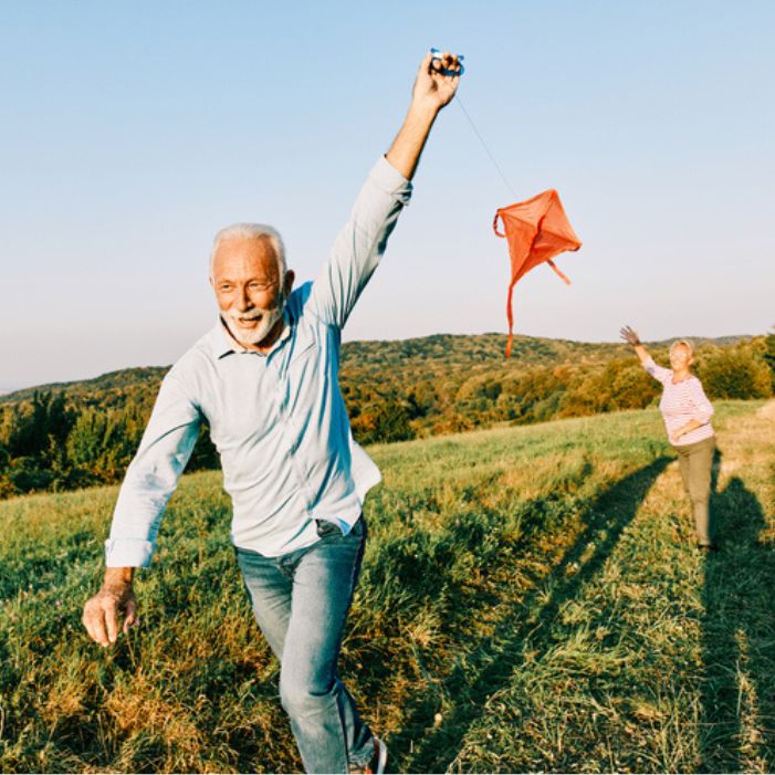 Two people flying a red kite in a grassy field.