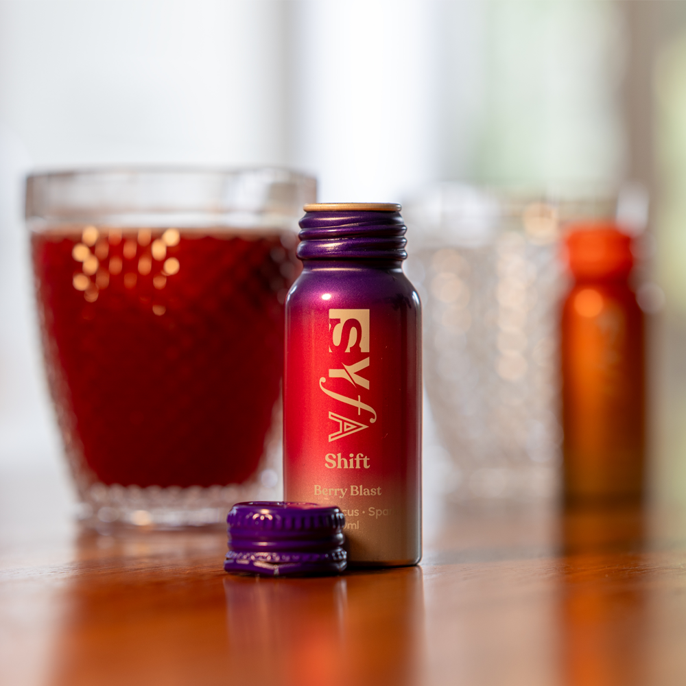 Colorful beverage bottle with glasses in the background on a wooden surface.
