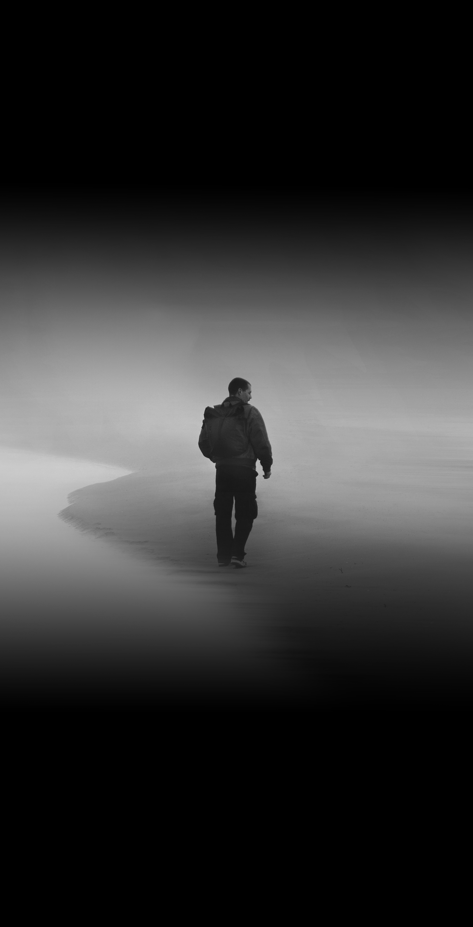 Person walking alone on a foggy beach.