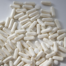 An overhead shot of a scattered pile of white capsules and round tablets on a plain surface.