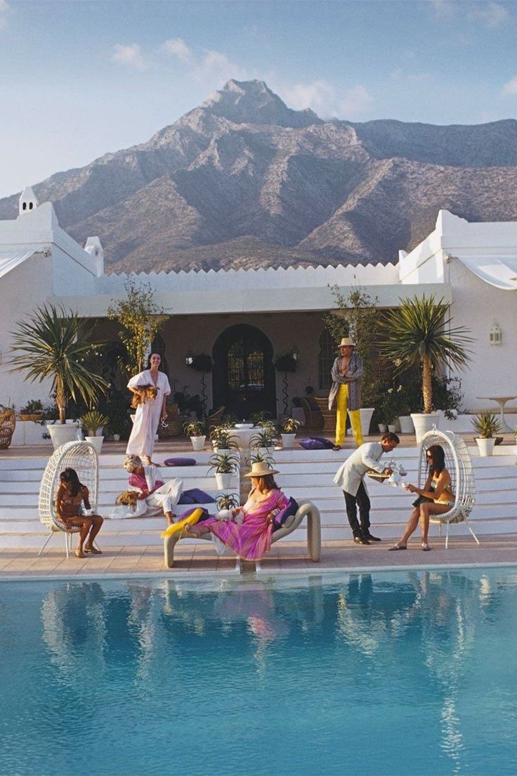 People relaxing by a pool with mountains in the background.