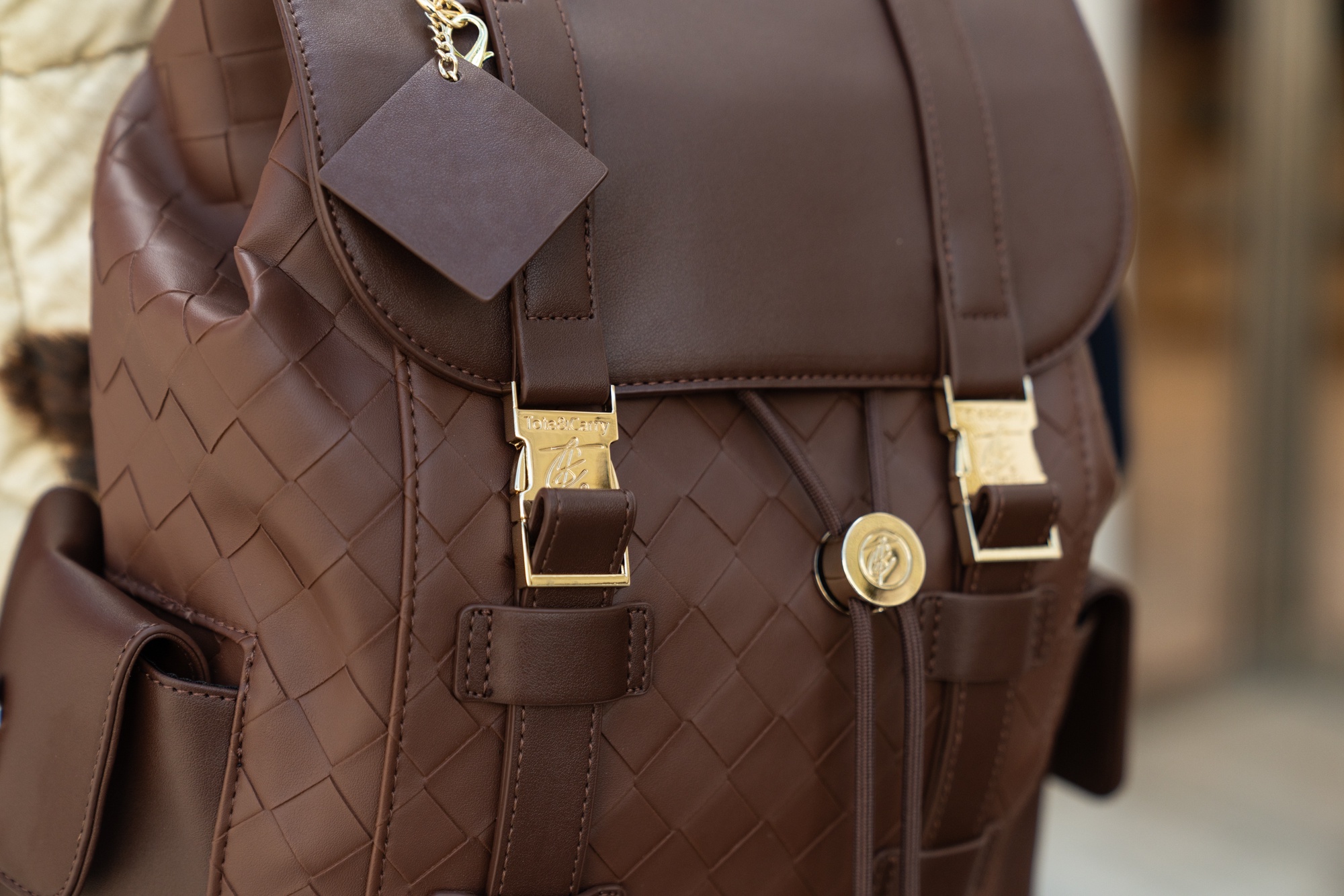A close-up of a brown woven-style backpack with gold-colored buckles and hardware.