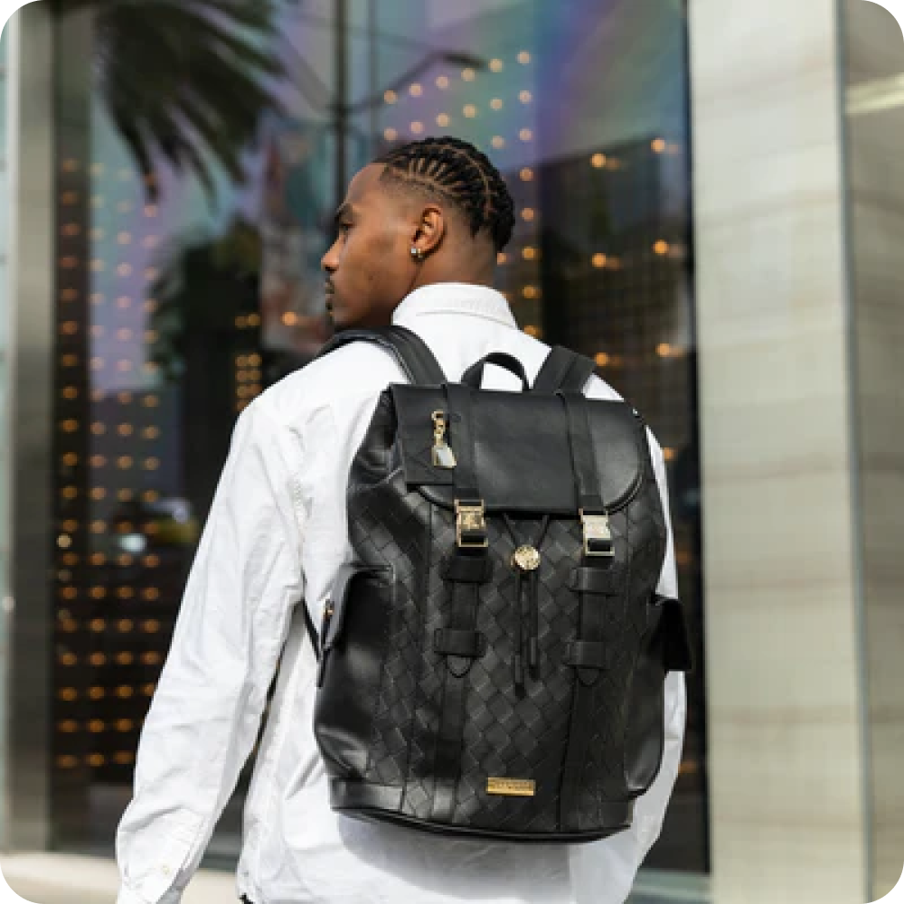 A man with cornrows wearing a white shirt and a black patterned backpack, seen from behind.