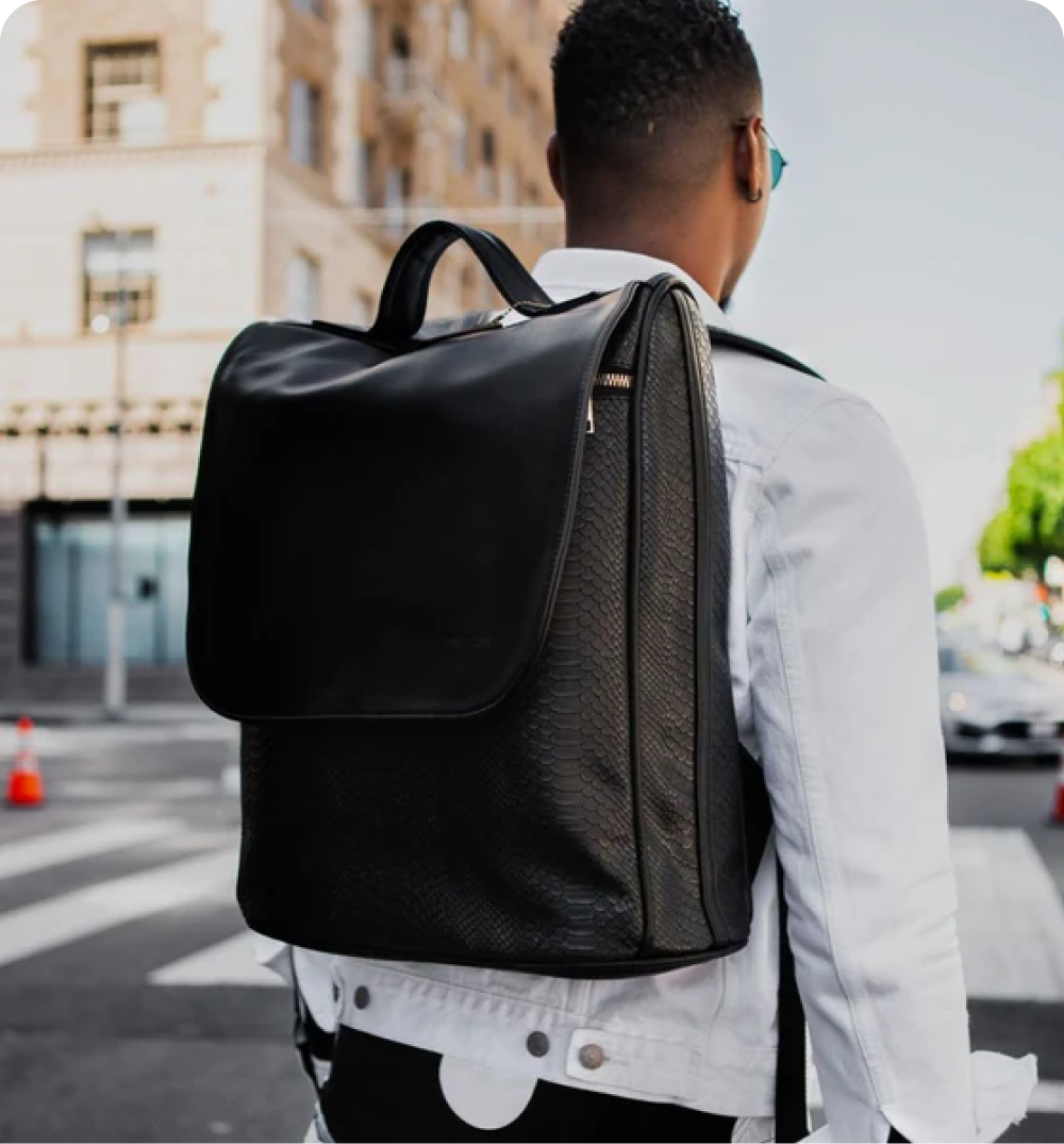 Rear view of a person wearing a white jacket and a black textured backpack on a city street.
