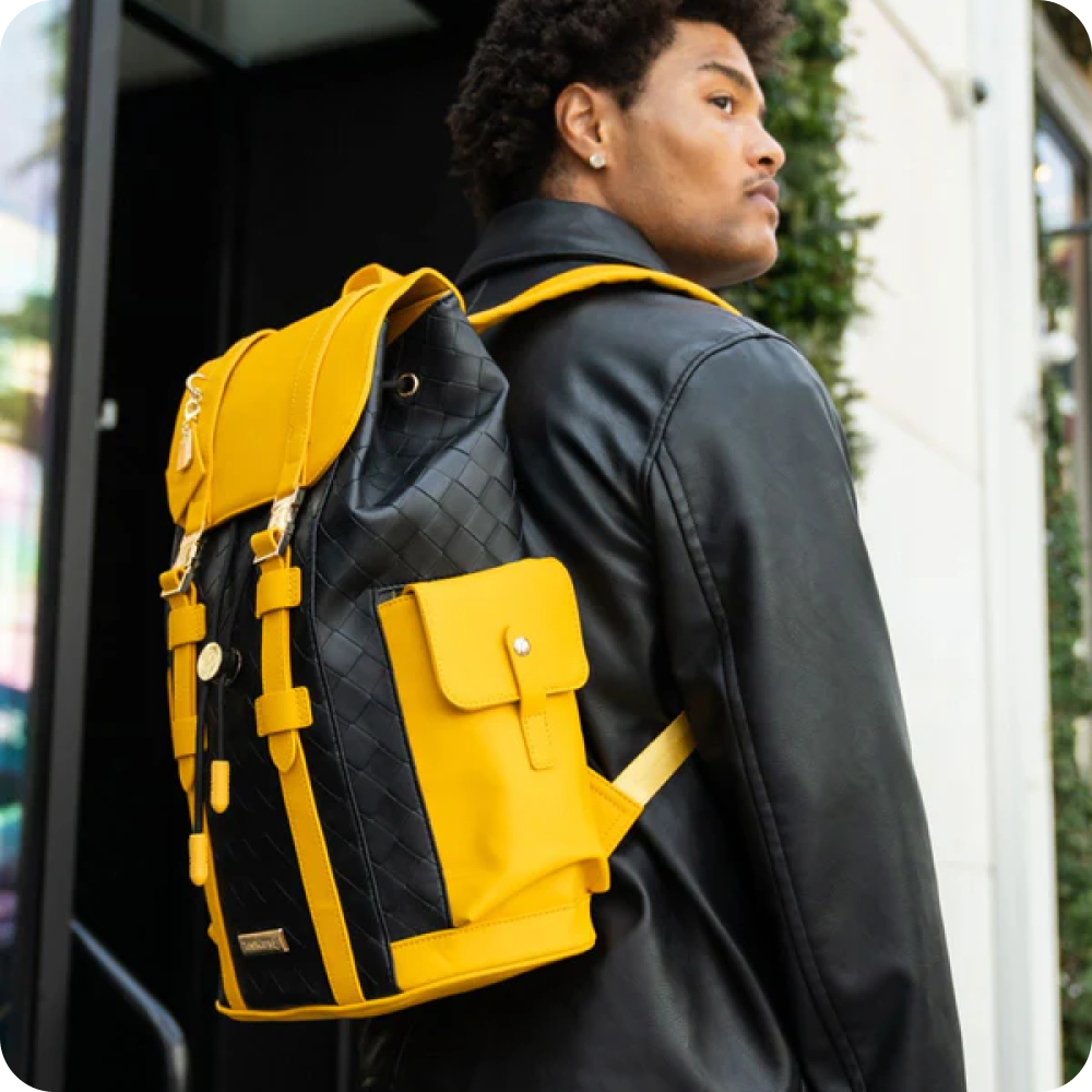 A man in a black leather jacket looks over his shoulder, wearing a black and yellow backpack.