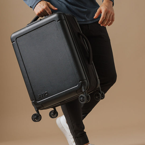 A person in a blue shirt and black pants holds a black, hardshell rolling suitcase.