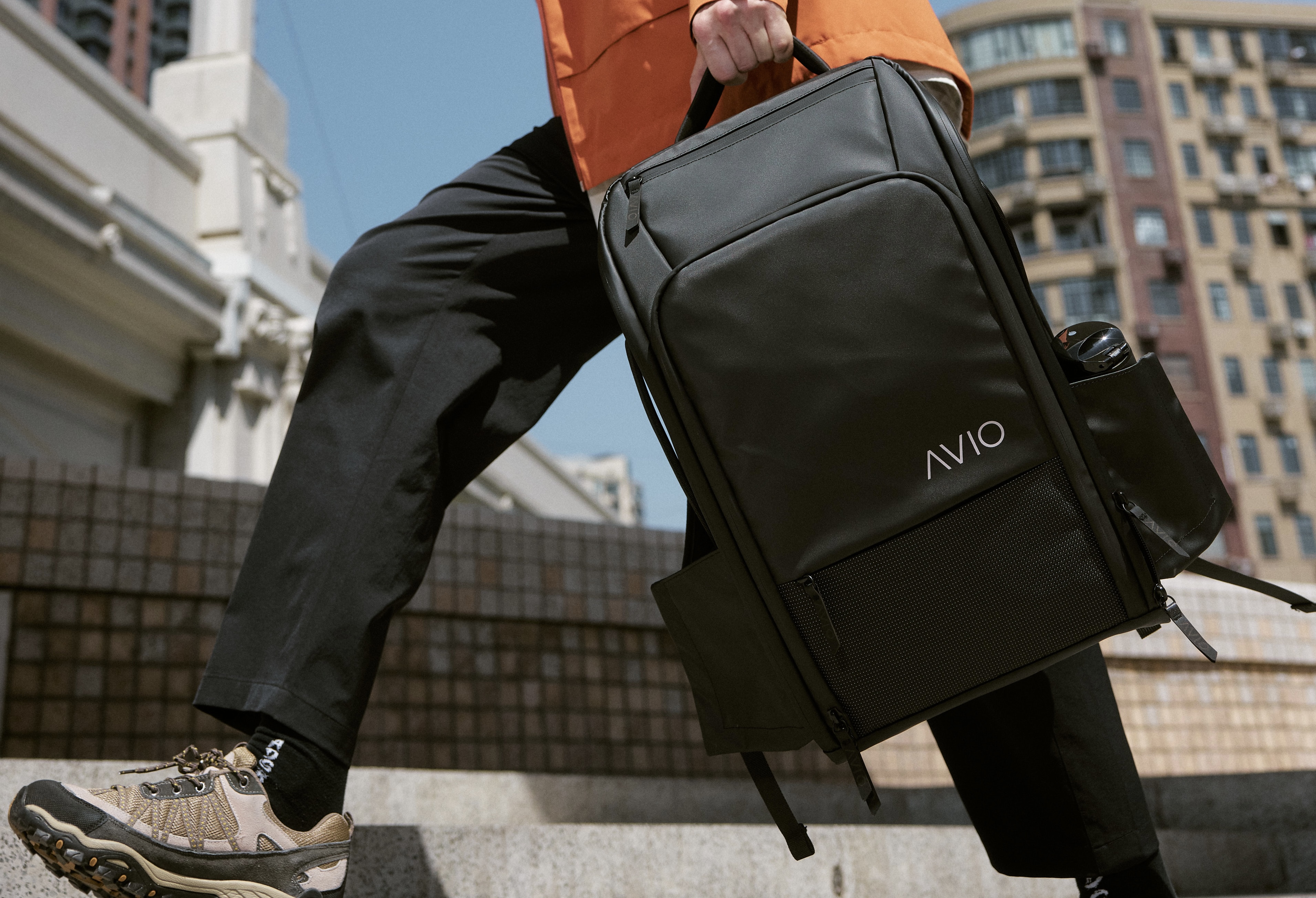 Person walking with a black AVIO backpack in an urban setting.