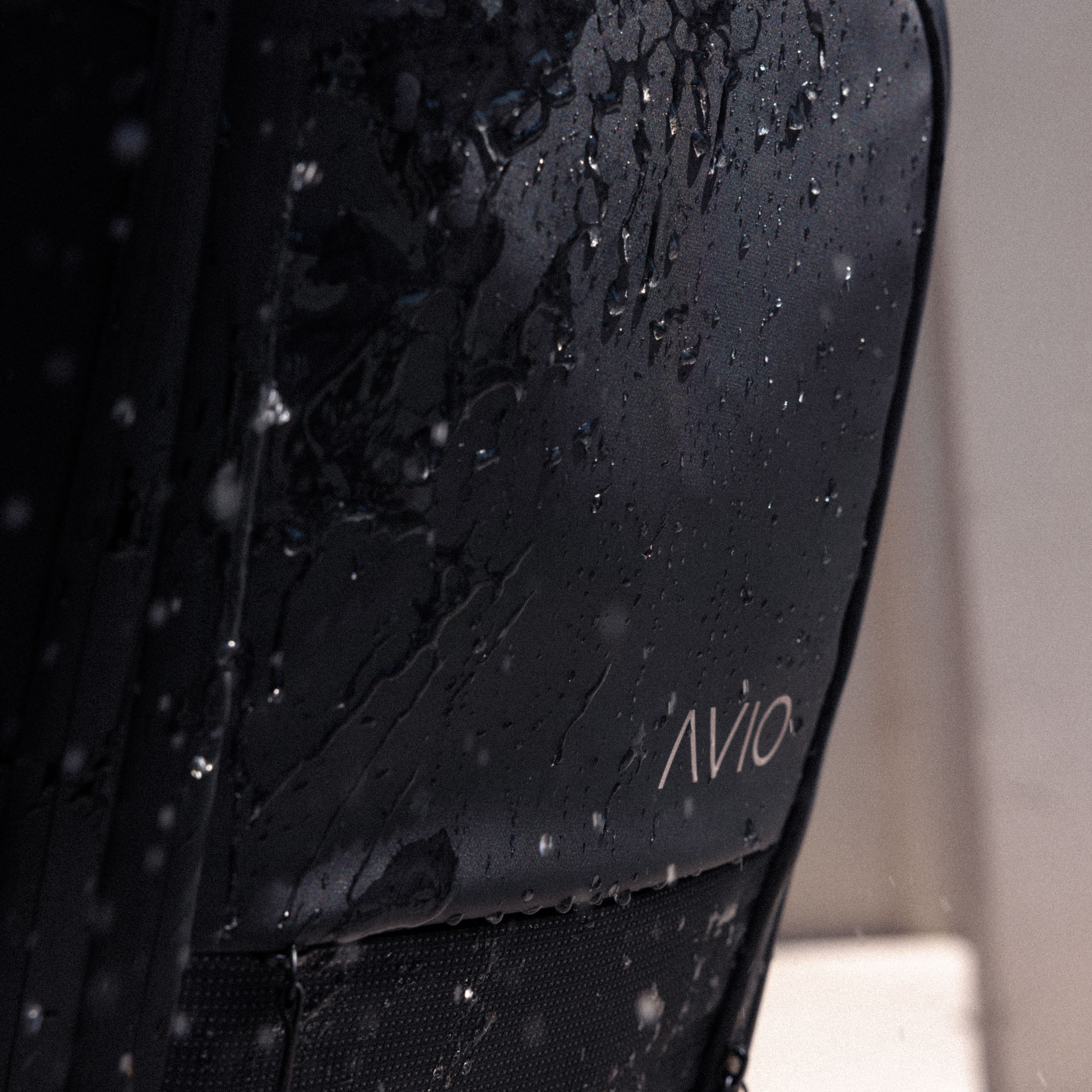 Close-up of a wet black backpack with 'AVIO' logo.