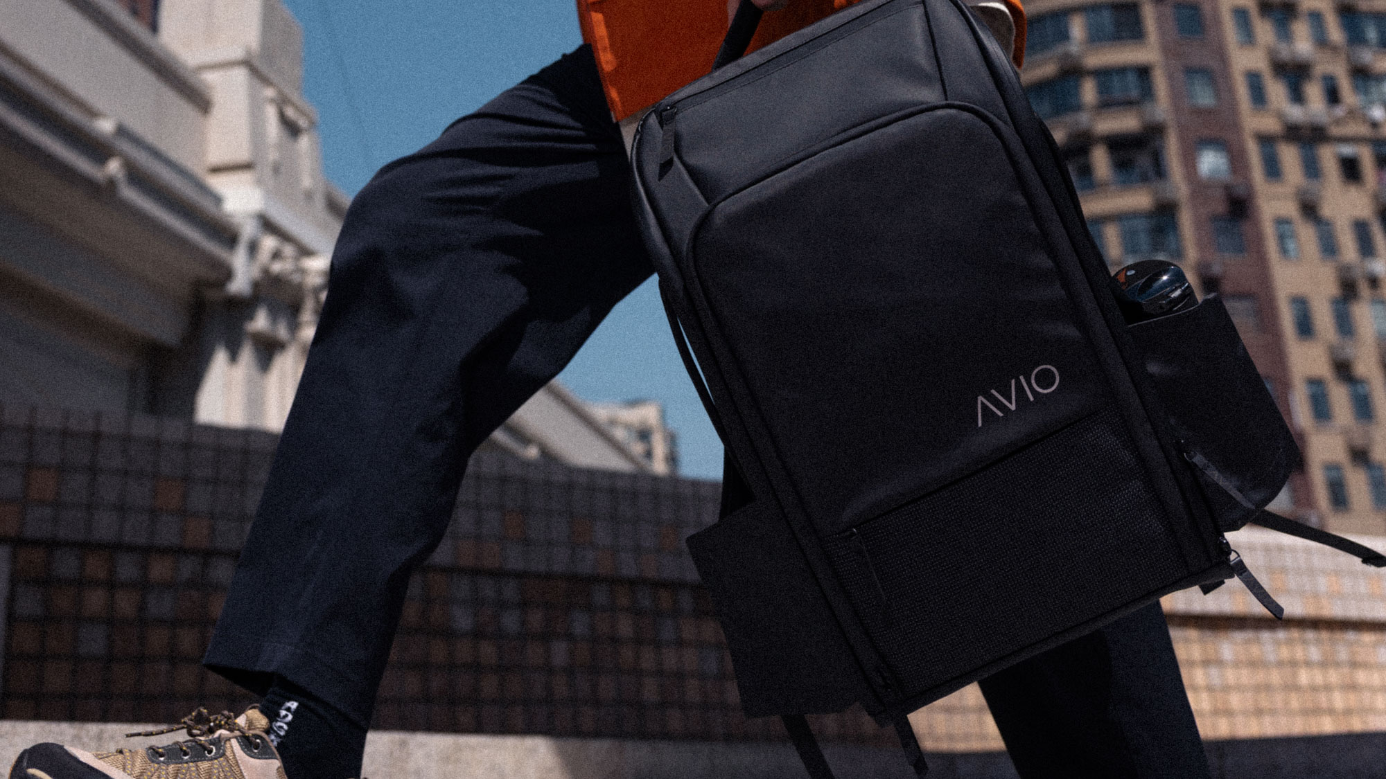 Person carrying a black AVIO backpack in an urban setting.
