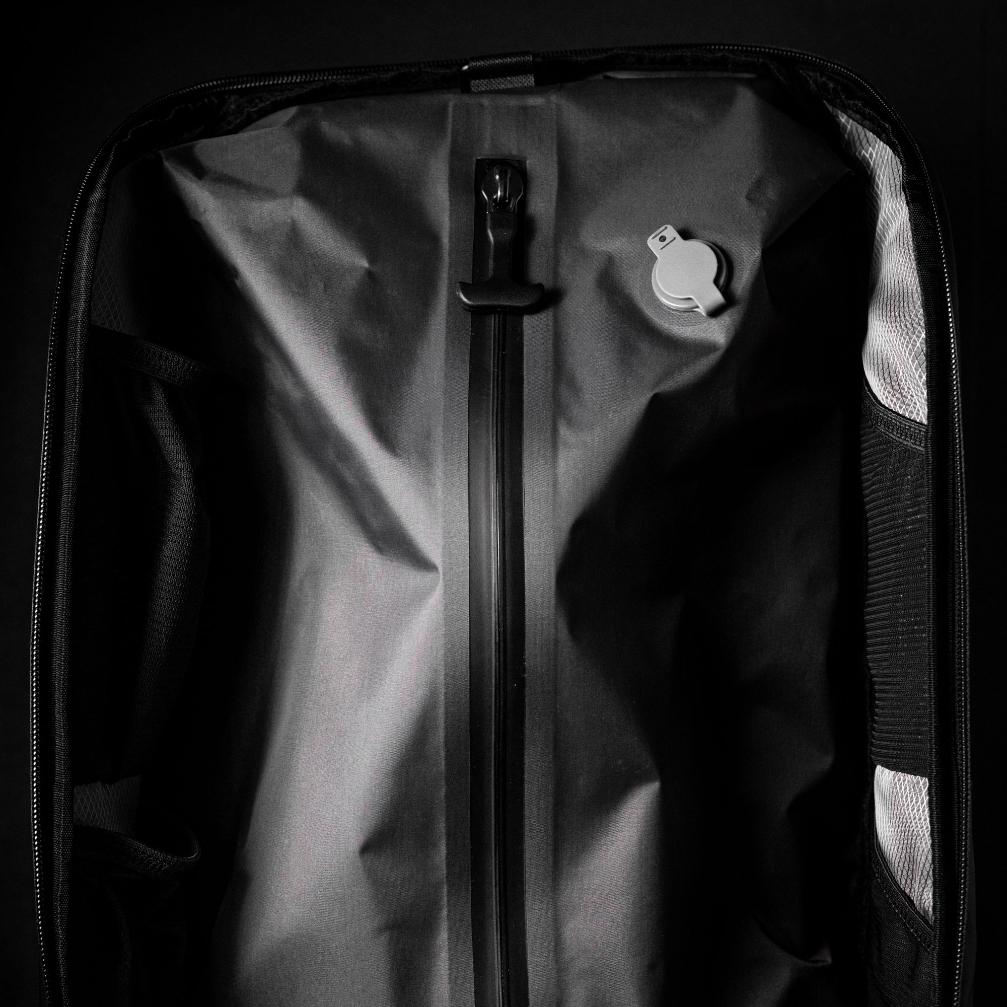 Open black suitcase with a zipper and a small round object inside.