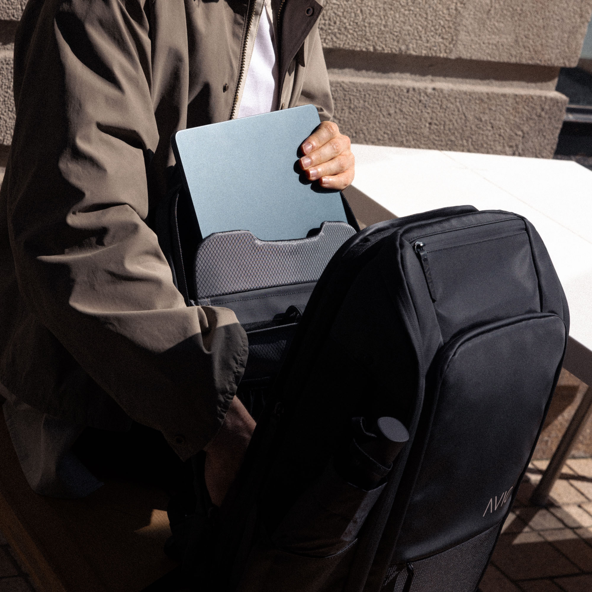 Person placing a laptop into a black backpack outdoors.
