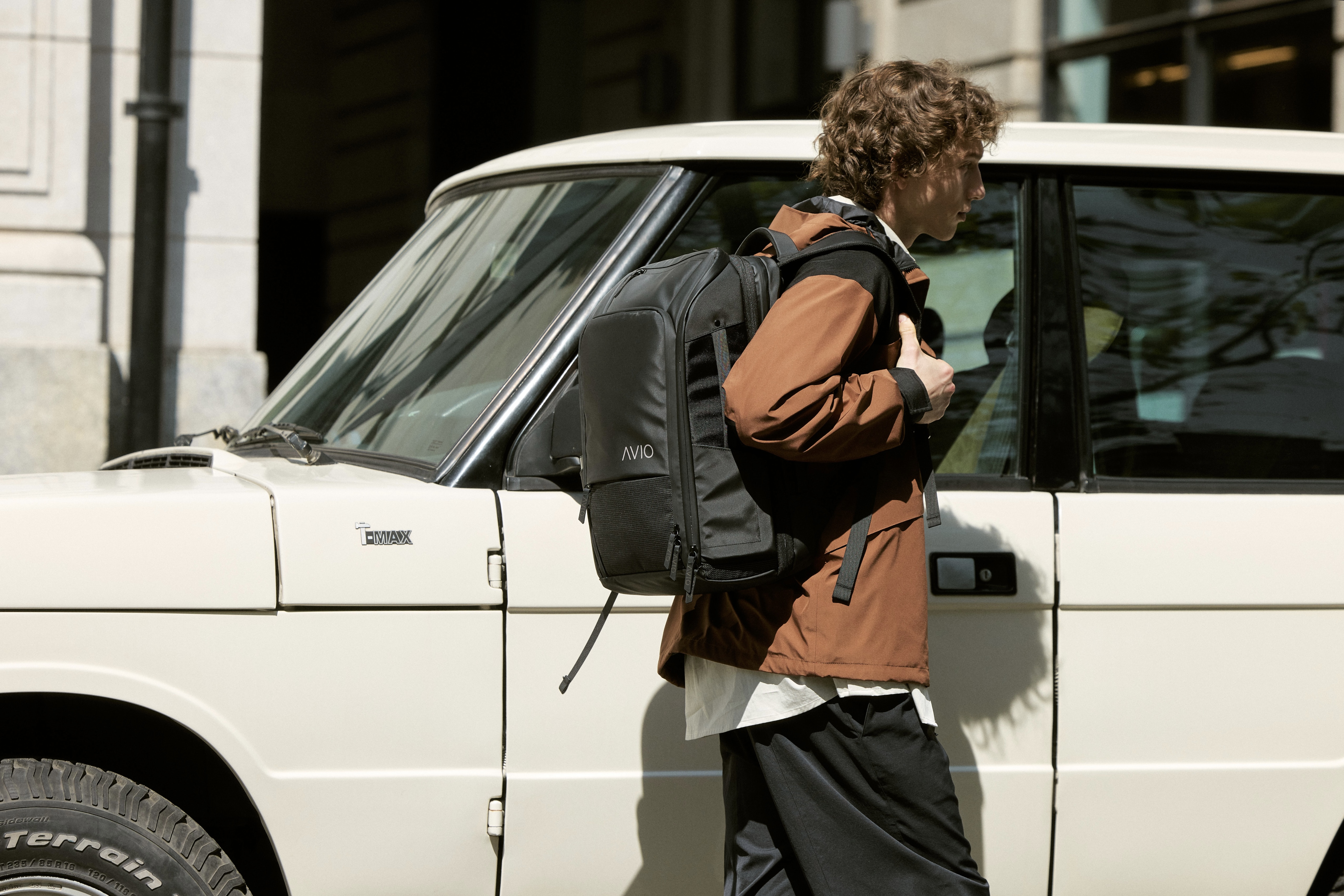 Person with backpack walking past a white SUV.