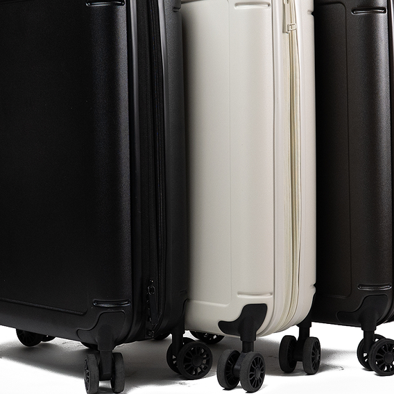 A close-up of the bottom of three rolling hard-shell suitcases, two black and one off-white.
