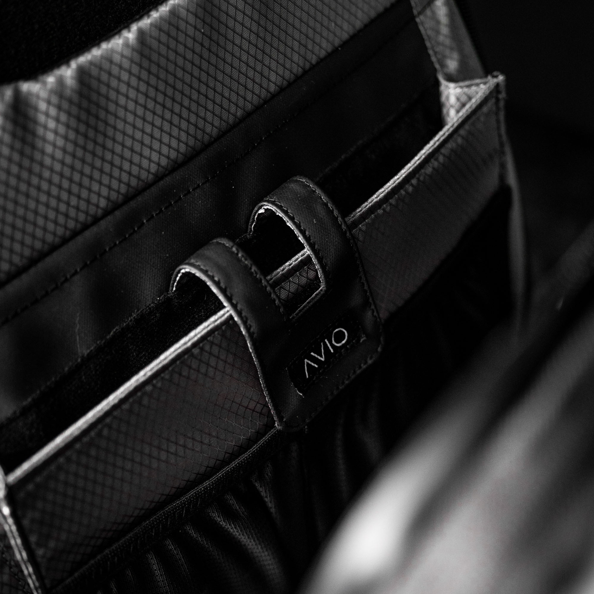 Close-up of a black textured bag with a strap labeled 'AVIO'.
