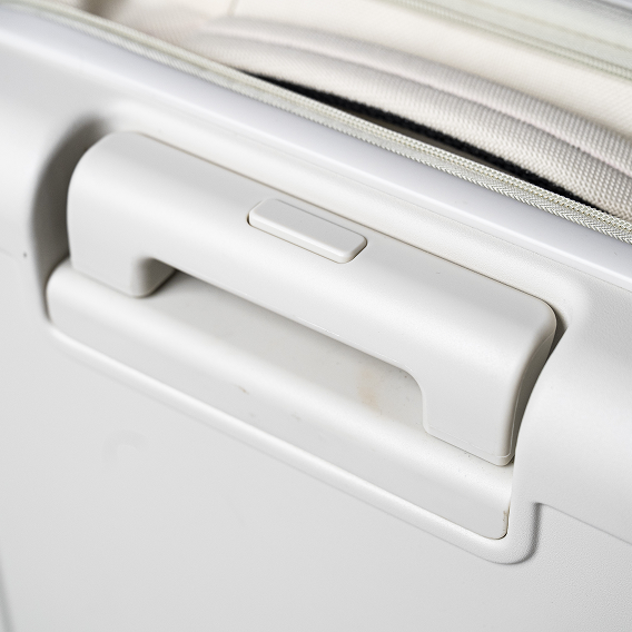 A close-up shot of a white suitcase's side handle with a button and a zipper.