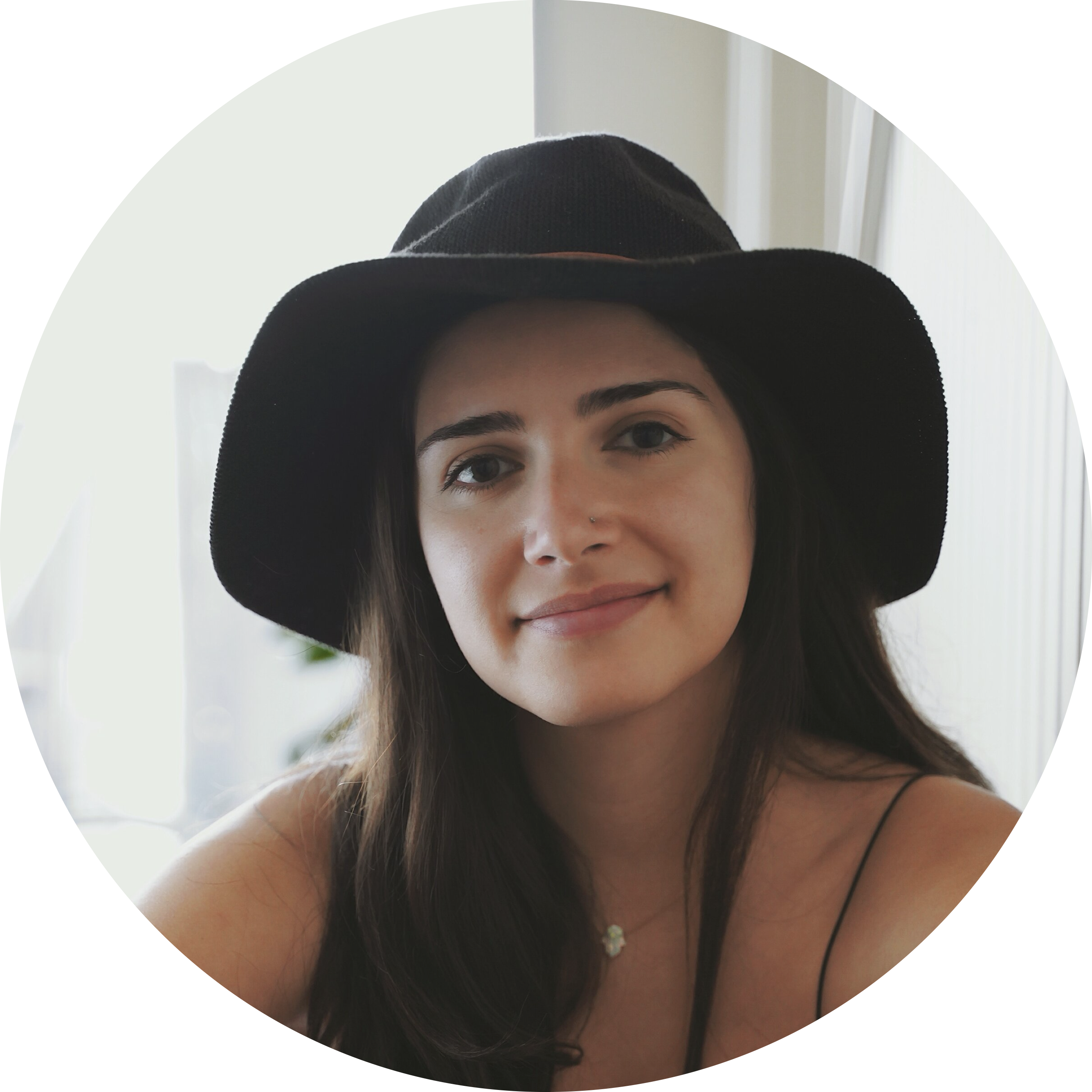 A person wearing a black wide-brimmed hat smiling softly indoors.