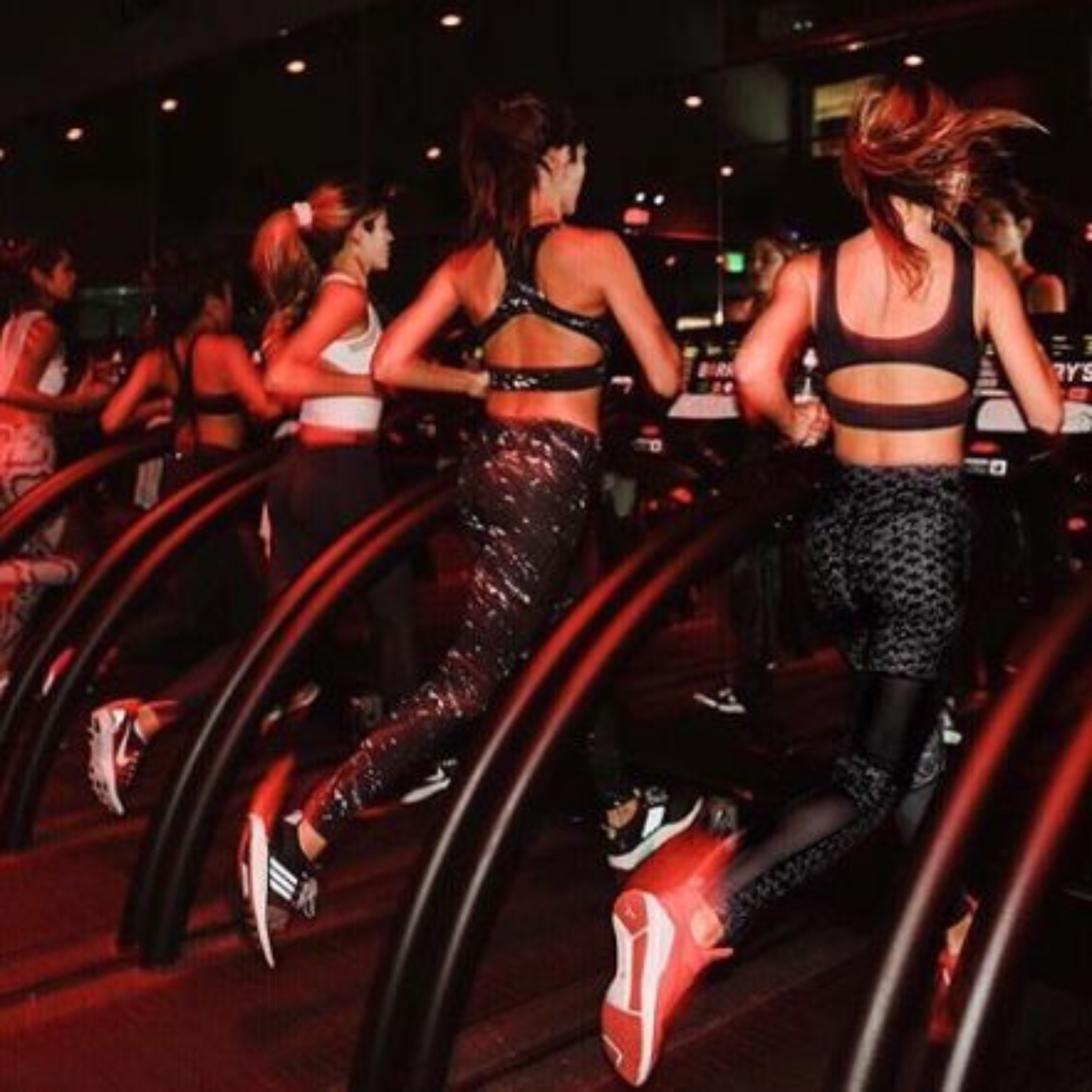 Group of women running on treadmills in a dimly lit gym.