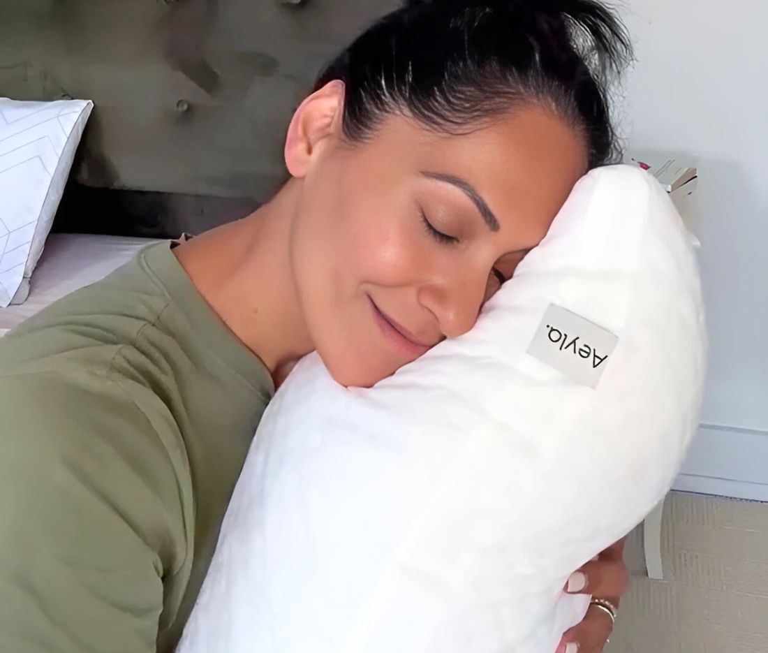 Person smiling and hugging a white pillow with a label.