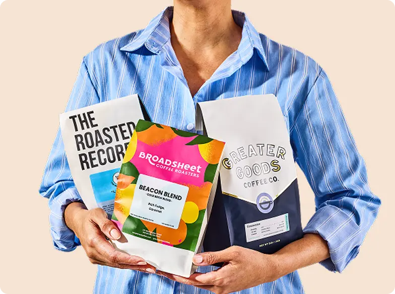 Person holding three bags of coffee from different brands.