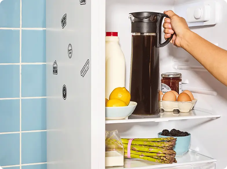 Open fridge with milk, lemons, pitcher, eggs, asparagus, and blackberries.