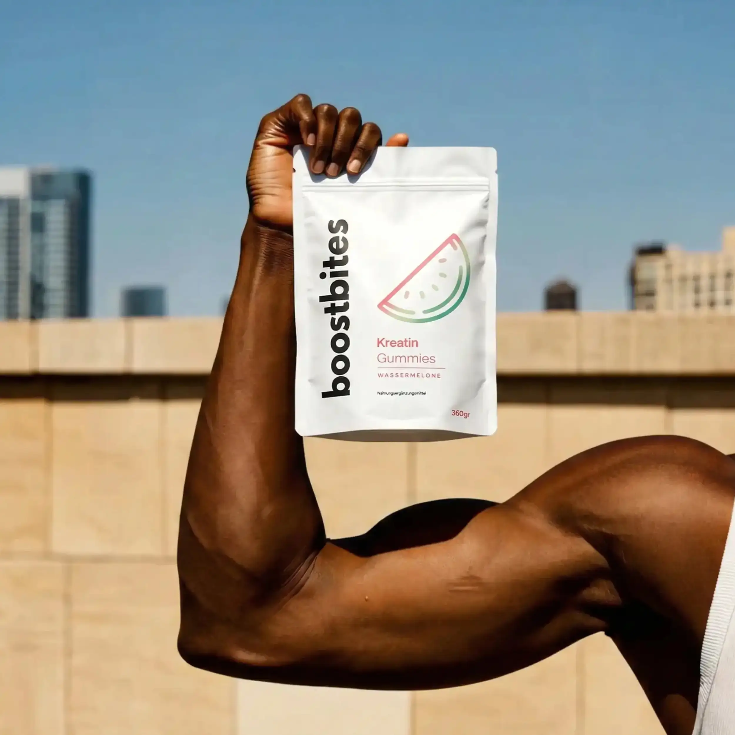 Muskulöser Arm hält BoostBites Kreatin Gummies Wassermelone – Kraft und Training
