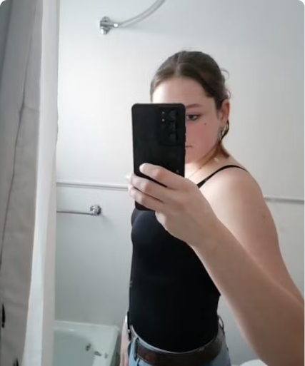 Person taking a mirror selfie in a bathroom, wearing a black top.