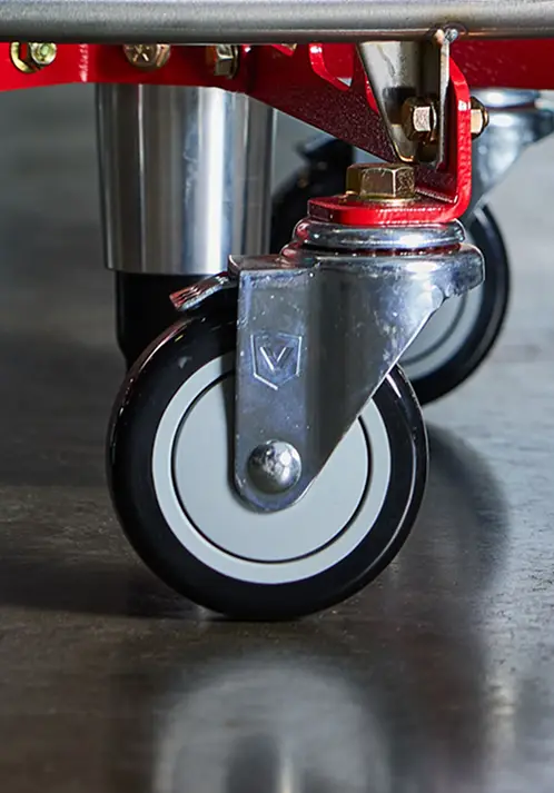 A close-up of a caster wheel with a chrome bracket bolted to a red metal frame.
