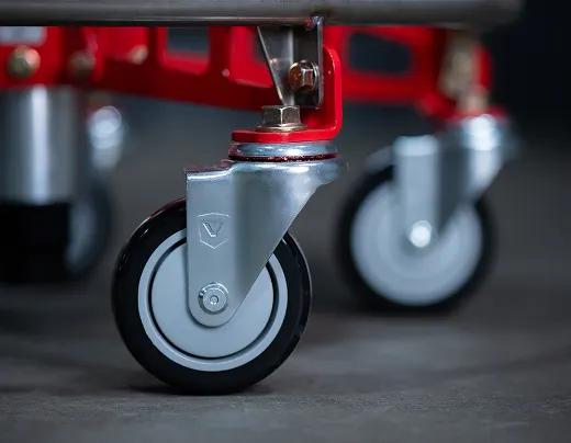 A close-up of a silver caster wheel with a black tire attached to a red metal frame.