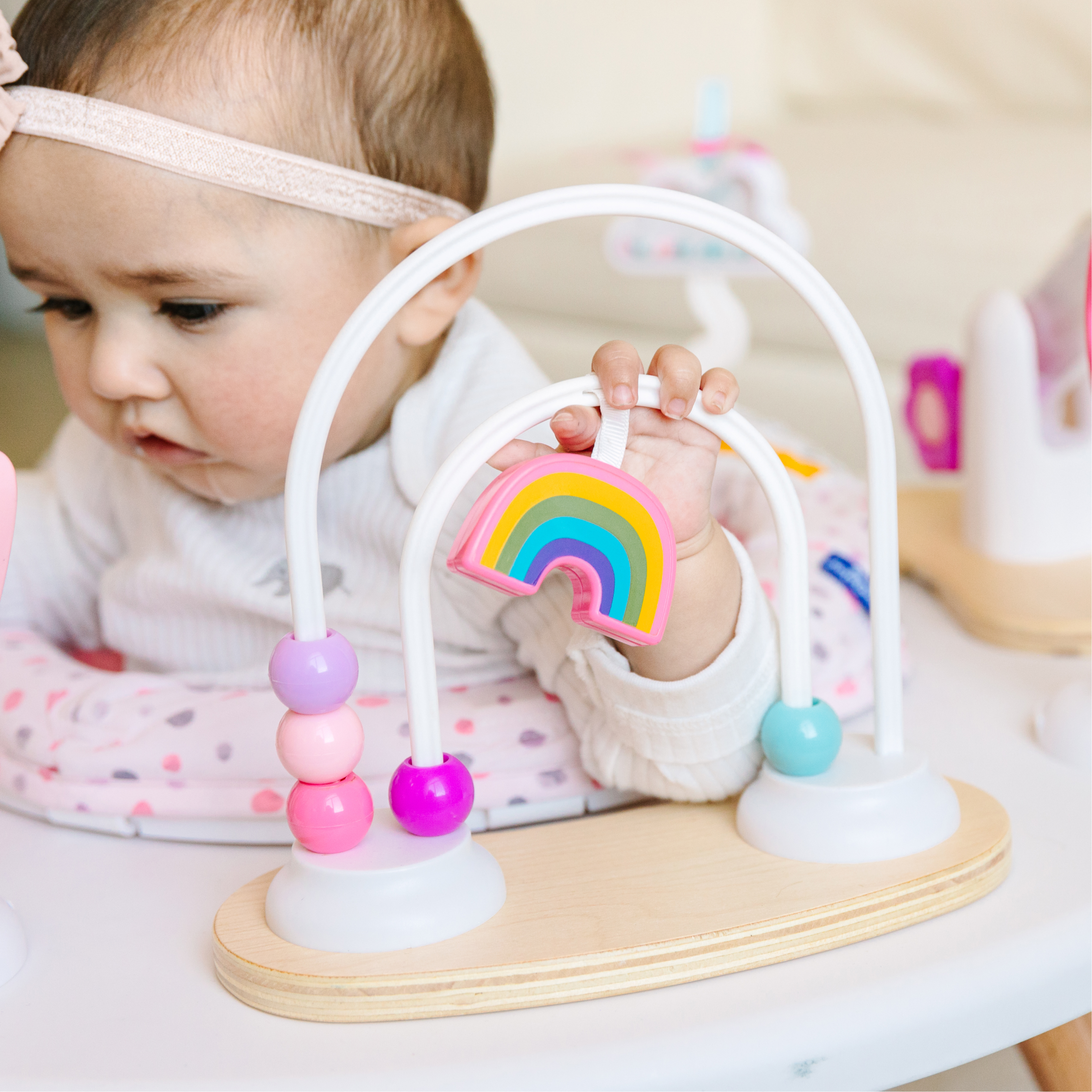 A baby girl in a highchair plays with a colorful bead maze toy with a rainbow.