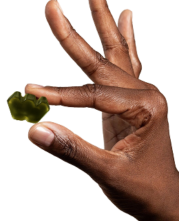 A person's hand with dark skin holding a single green, W-shaped gummy candy.