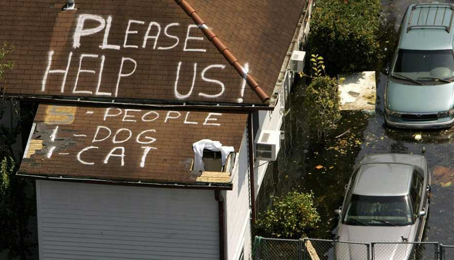 Roof with 'Please help us!' message next to flooded area and cars.
