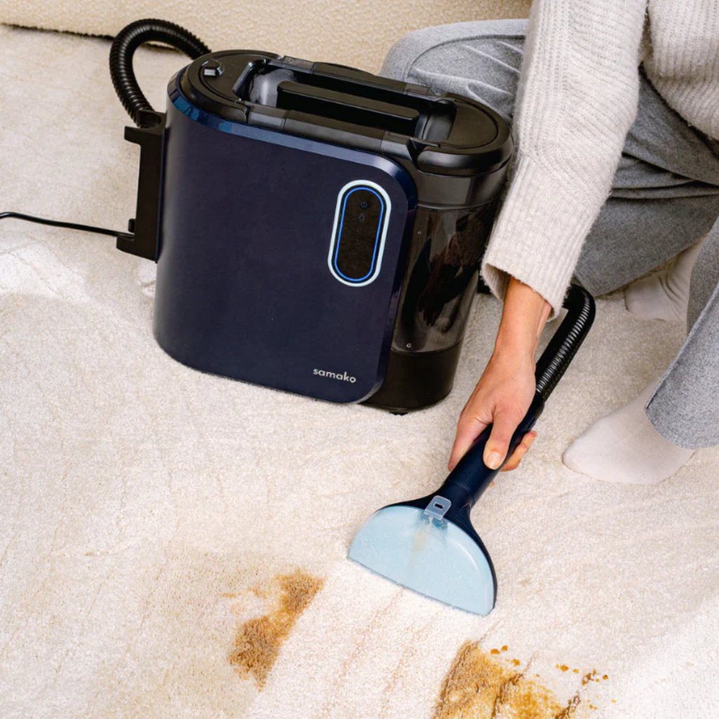 A person uses a portable spot cleaner to remove a stain from a light-colored carpet.