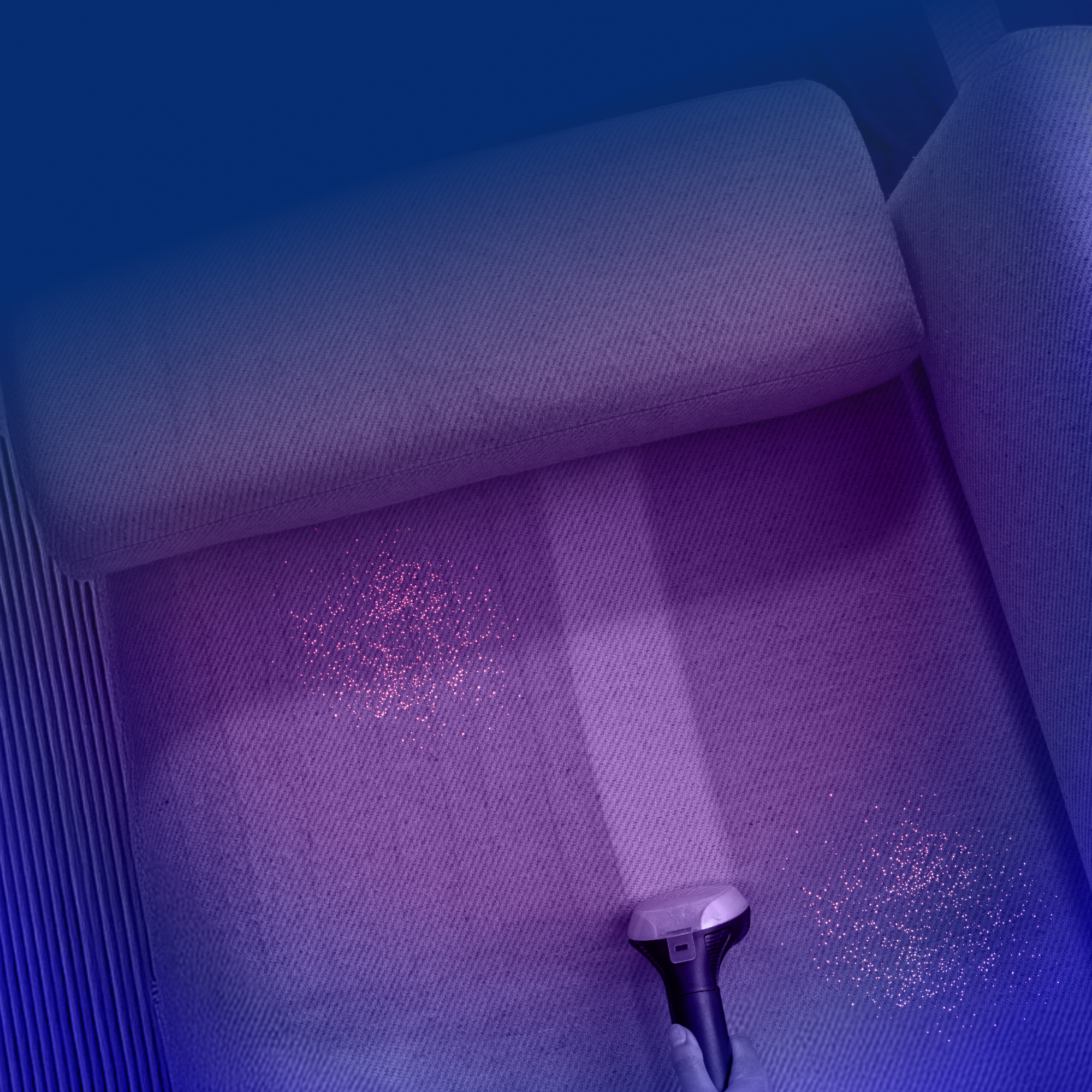 An overhead view of a person using a handheld vacuum to clean a purple upholstered sofa.