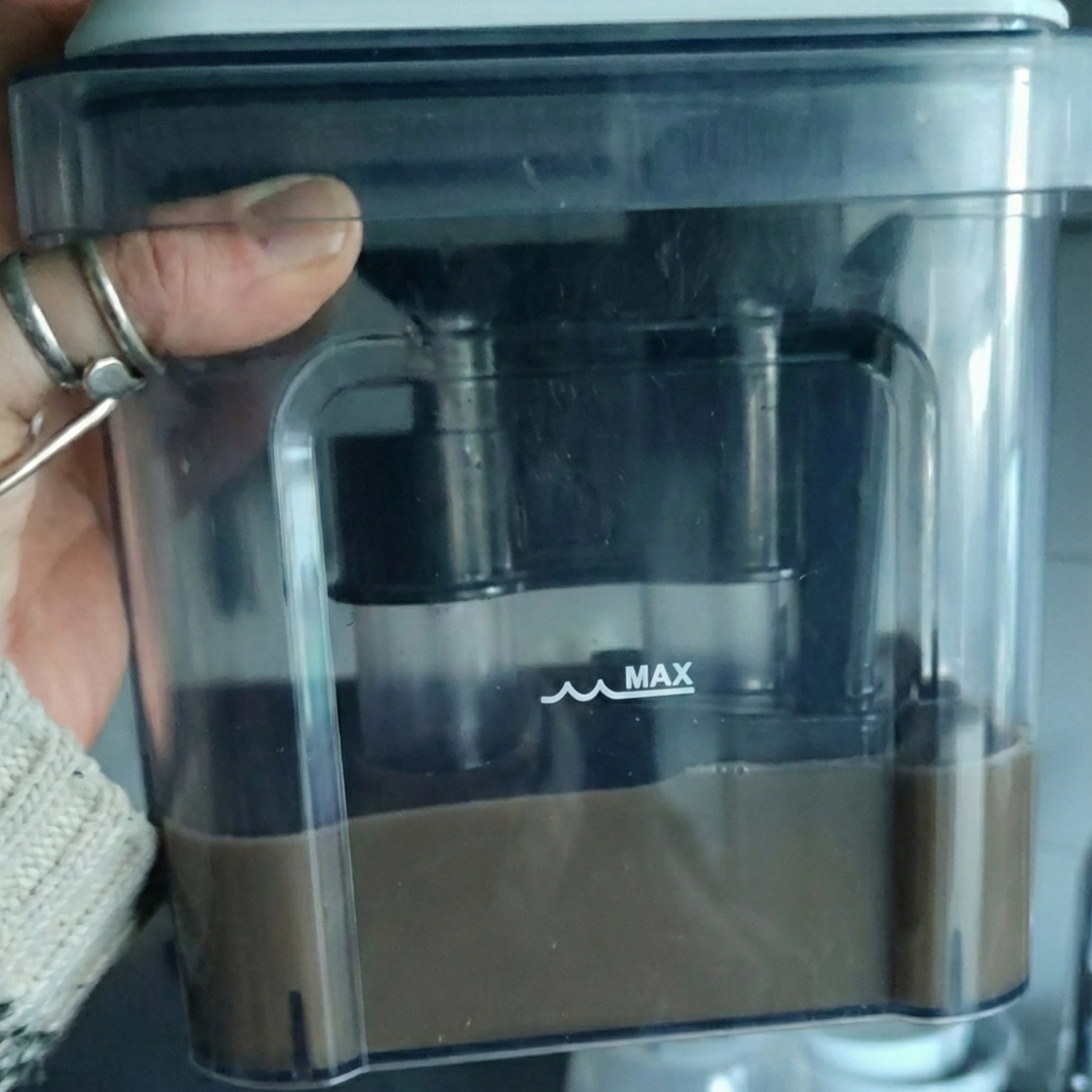 A person's hand holding a clear plastic container partially filled with a brown, opaque liquid.