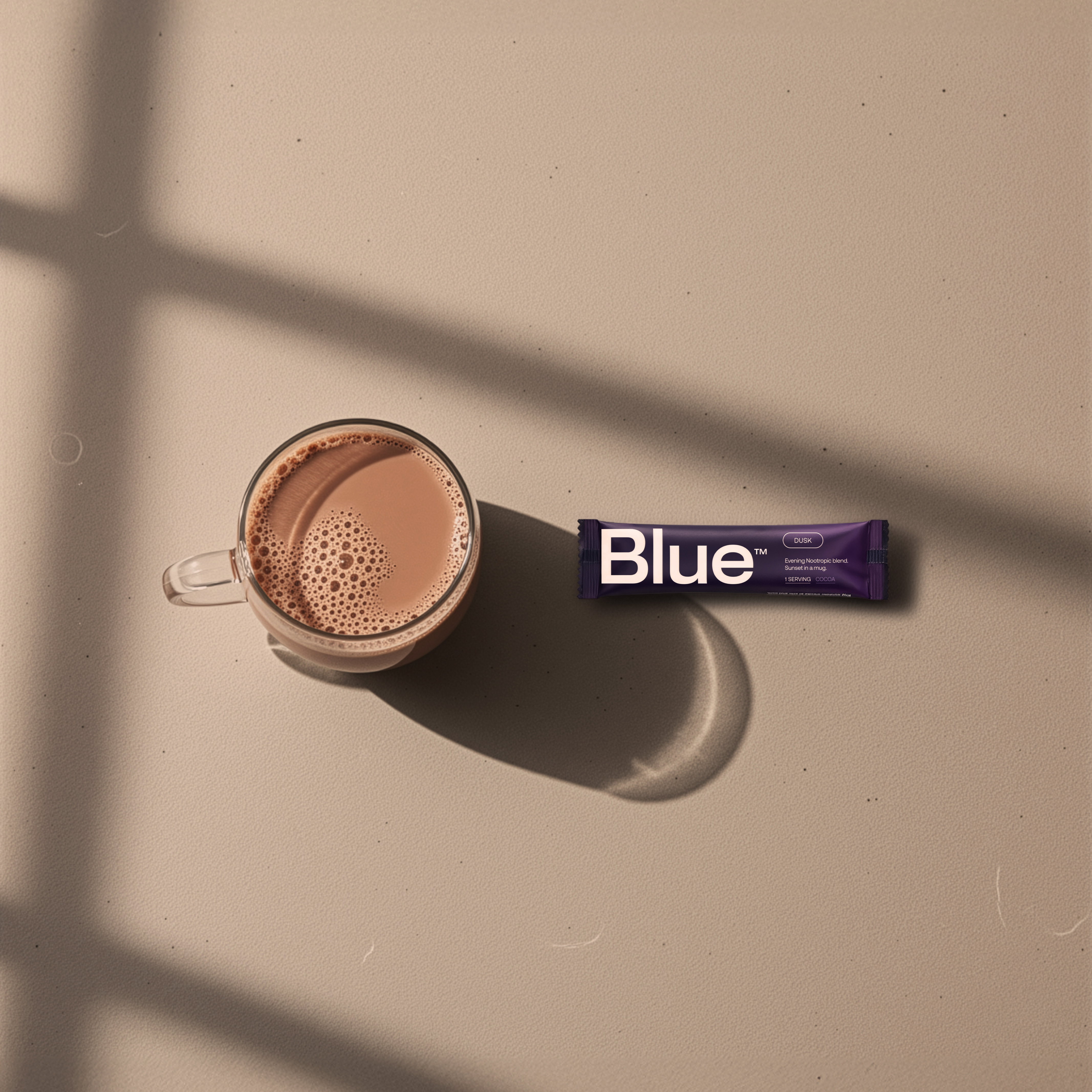 Glass cup of brown liquid and purple 'Blue' packet on beige surface.