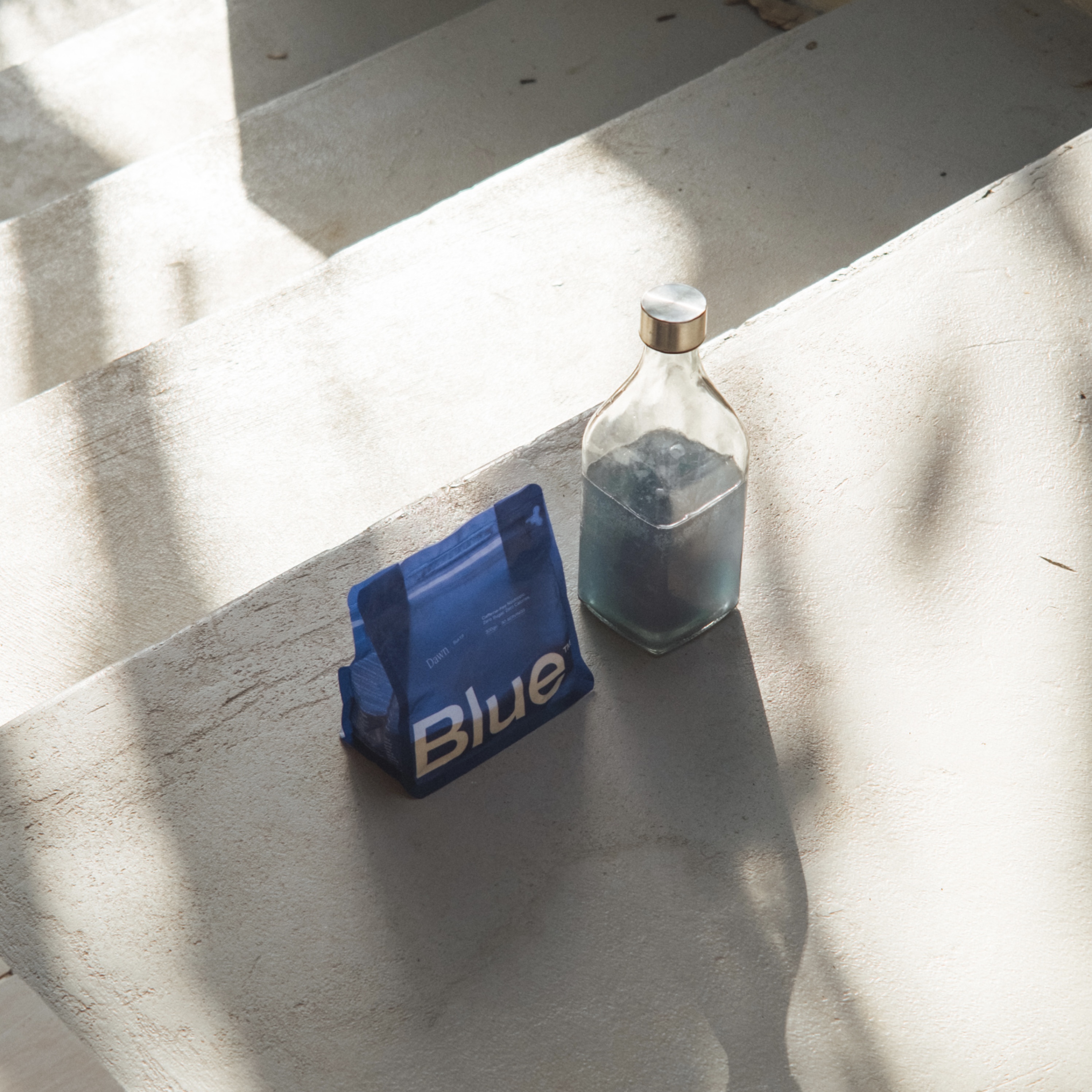 Blue package and glass bottle on sunlit concrete steps.