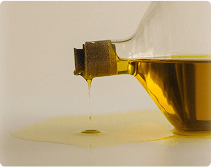 A glass bottle with cork, leaking golden liquid onto a surface.