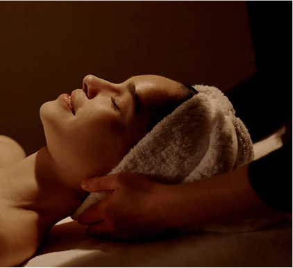 Person receiving a relaxing facial massage with a towel wrapped around their head.