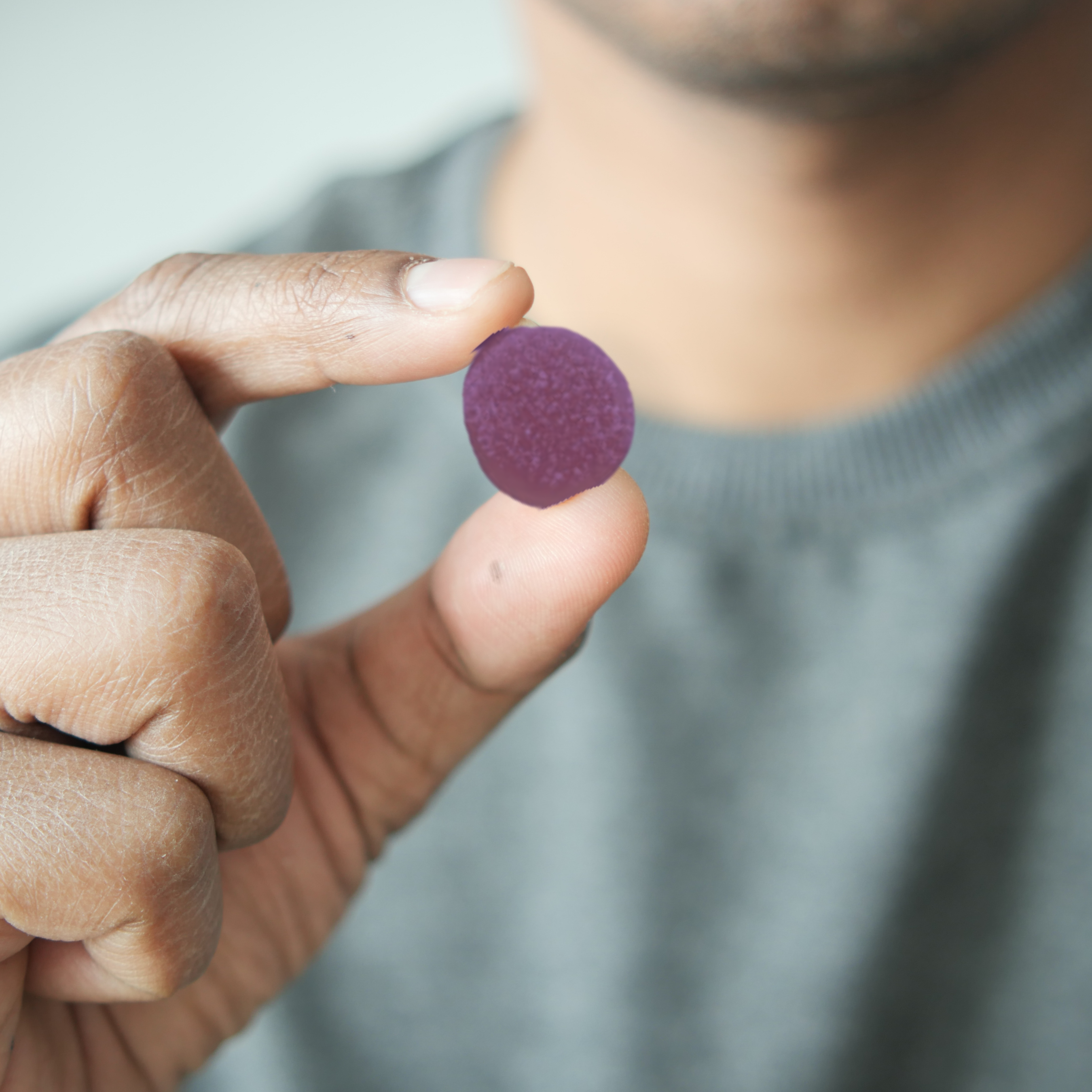 Person holding a small purple candy between fingers.