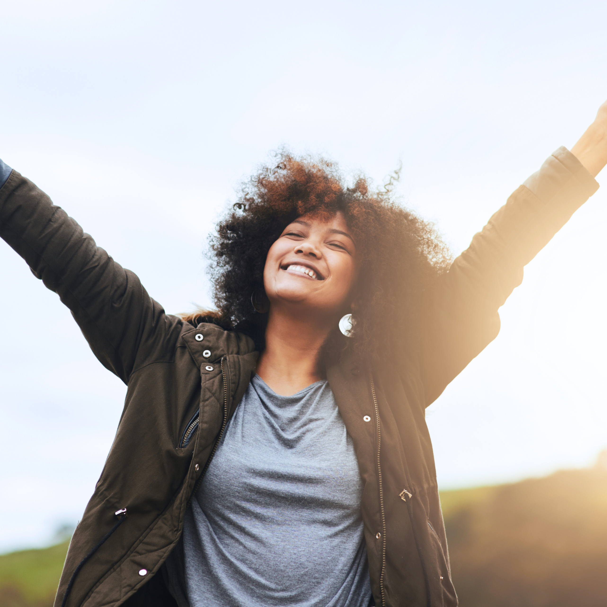 Person smiling with arms raised outdoors.