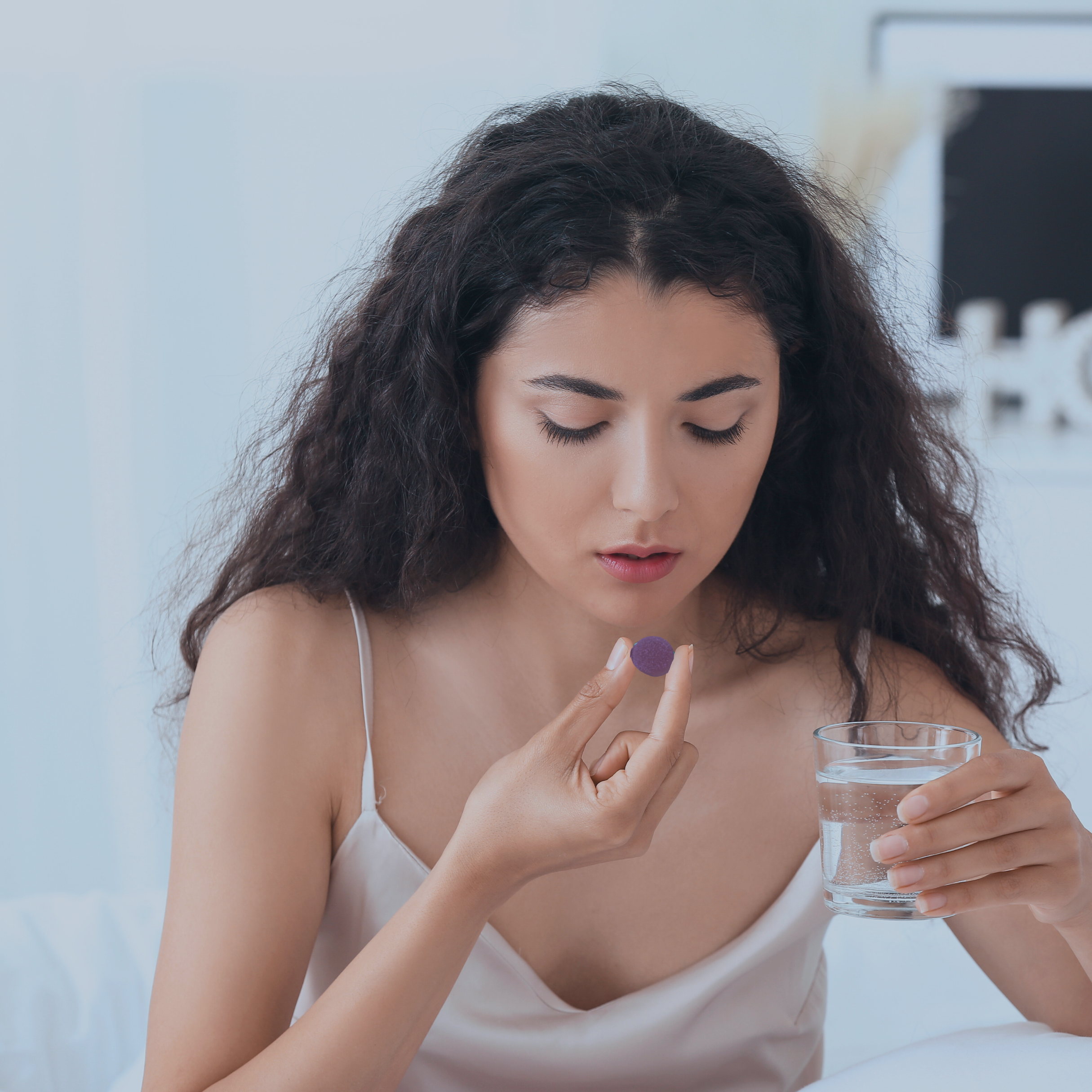 Woman holding a purple pill and a glass of water.