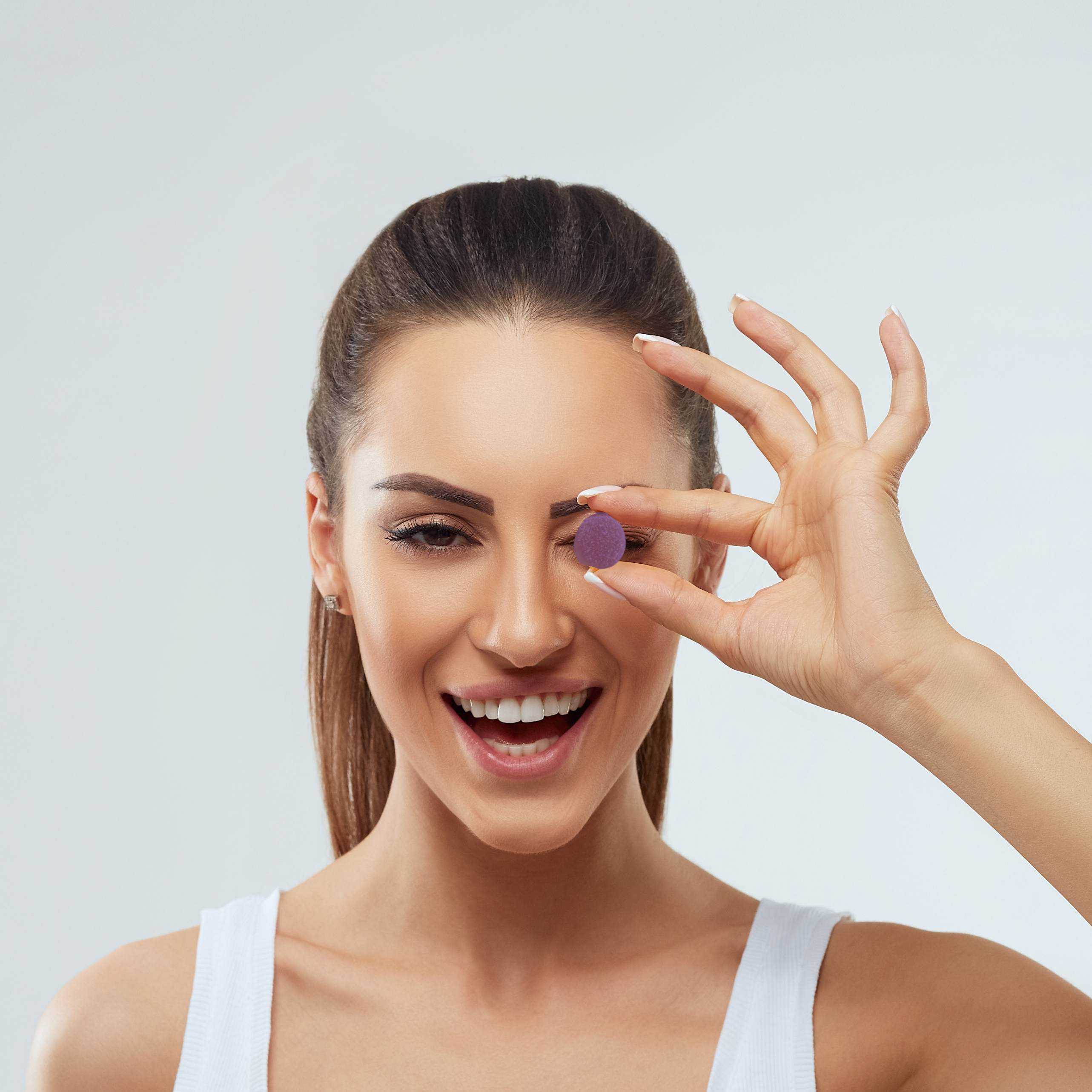 Person holding a purple gummy candy between fingers, smiling in the background.