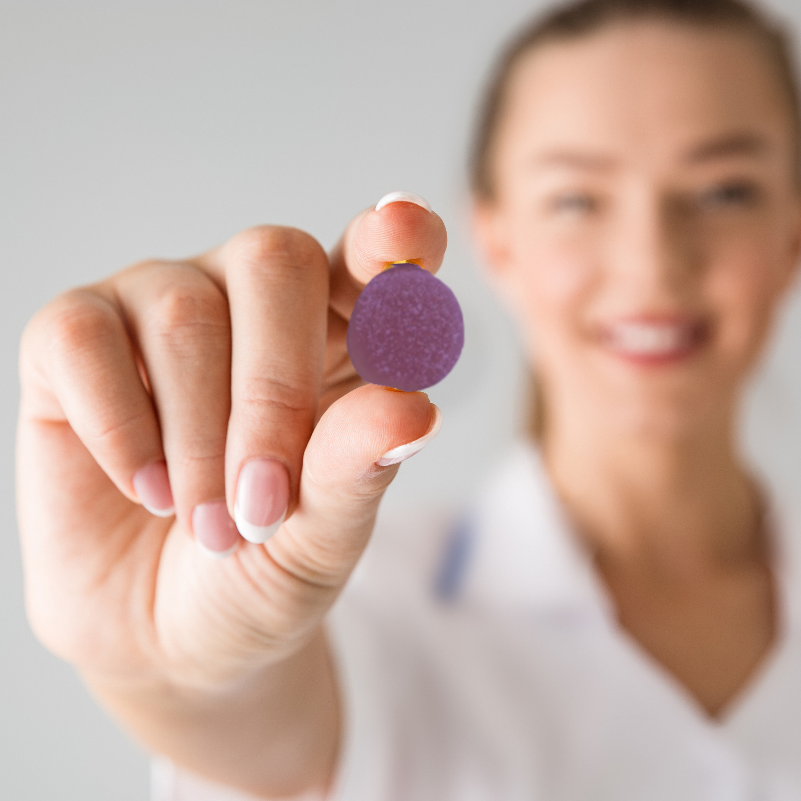 Person holding a purple gummy candy between fingers, smiling in the background.