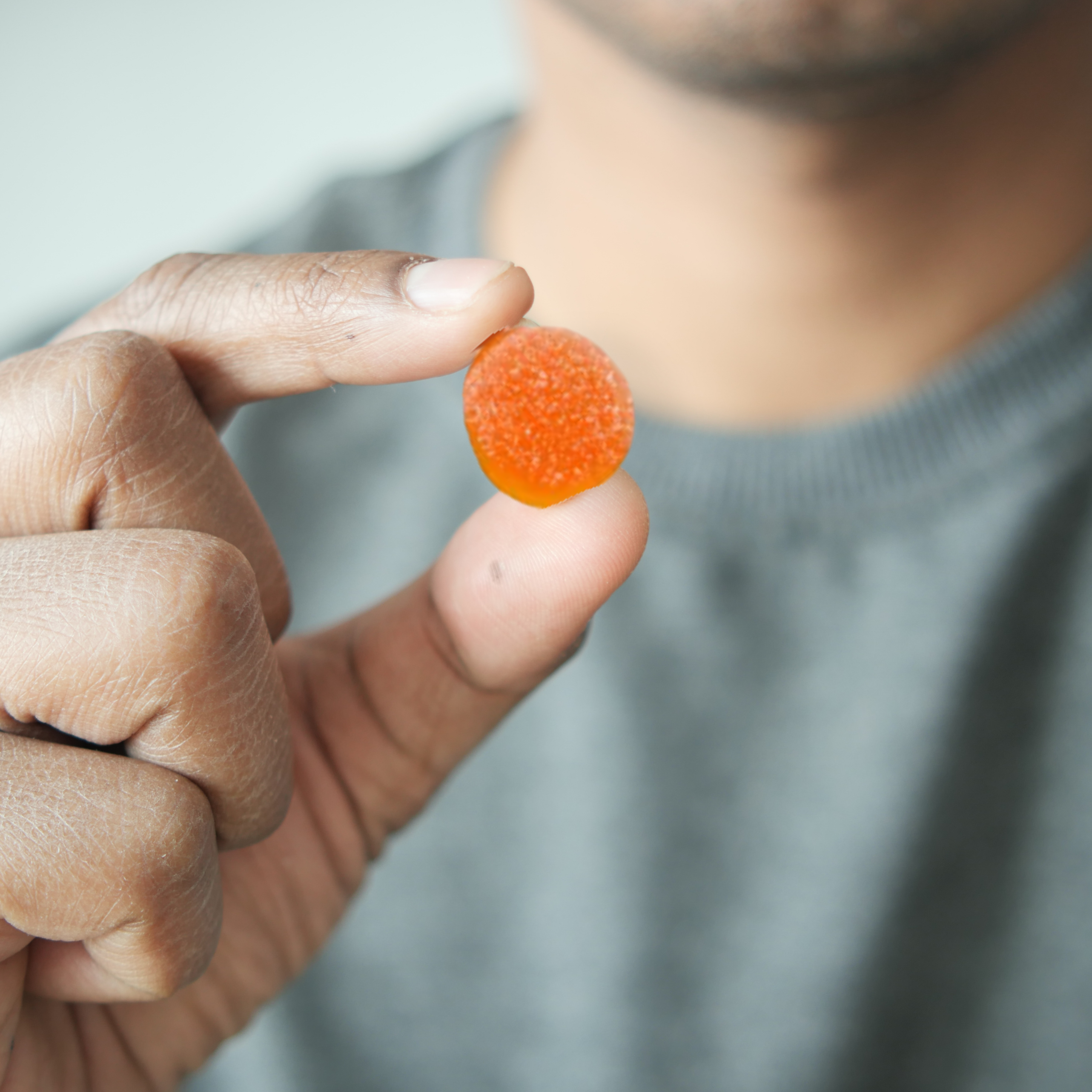Person holding an orange gummy candy between fingers.