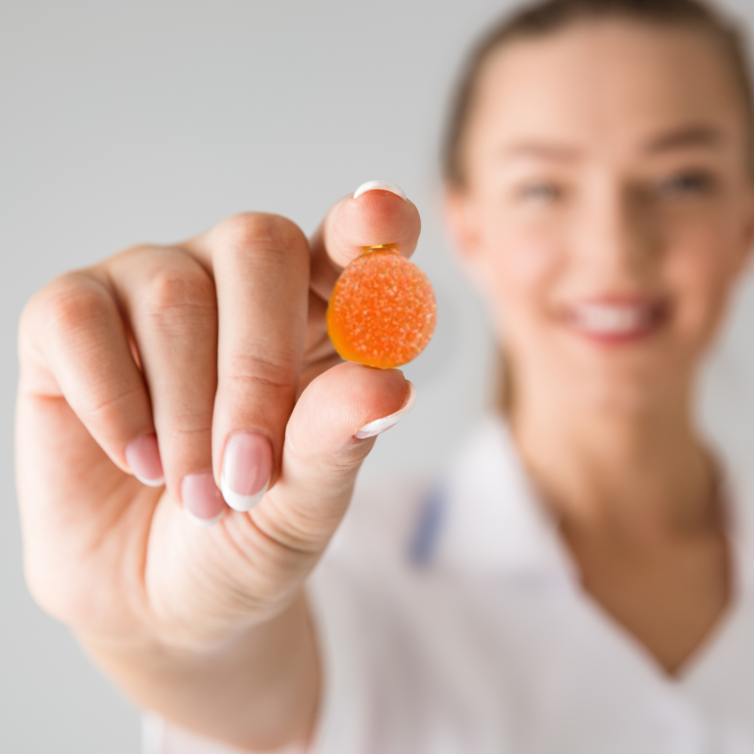 Person holding an orange gummy candy between fingers, smiling in the background.