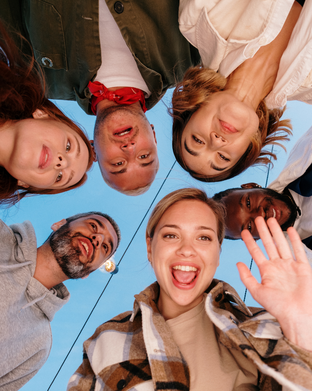 A low-angle view of six friends in a huddle, looking down and smiling at the camera.
