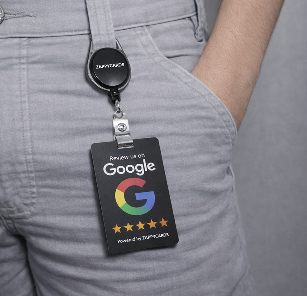A person wearing a Zappycards 'Review us on Google' badge clipped to their grey pants.