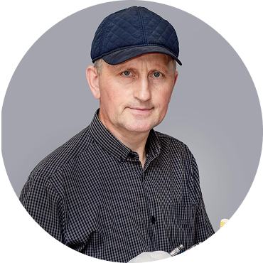 A man wearing a dark flat cap and a patterned shirt, looking at the camera.